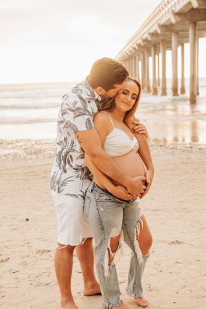 Intimate maternity photo of couple sharing tender moment on beach at sunset.
