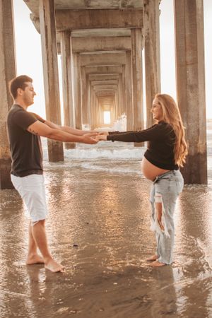 Couple holding hands under pier during golden hour photoshoot.