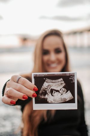 Close up of hands holding an ultrasound photo against a beach sunset backdrop.