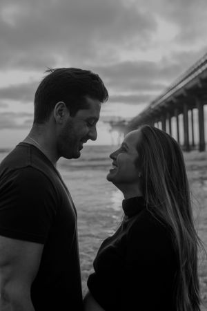 Romantic black and white portrait of couple by pier at sunset.