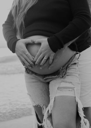 A close-up black and white photo showing hands cradling a pregnant belly against distressed denim.