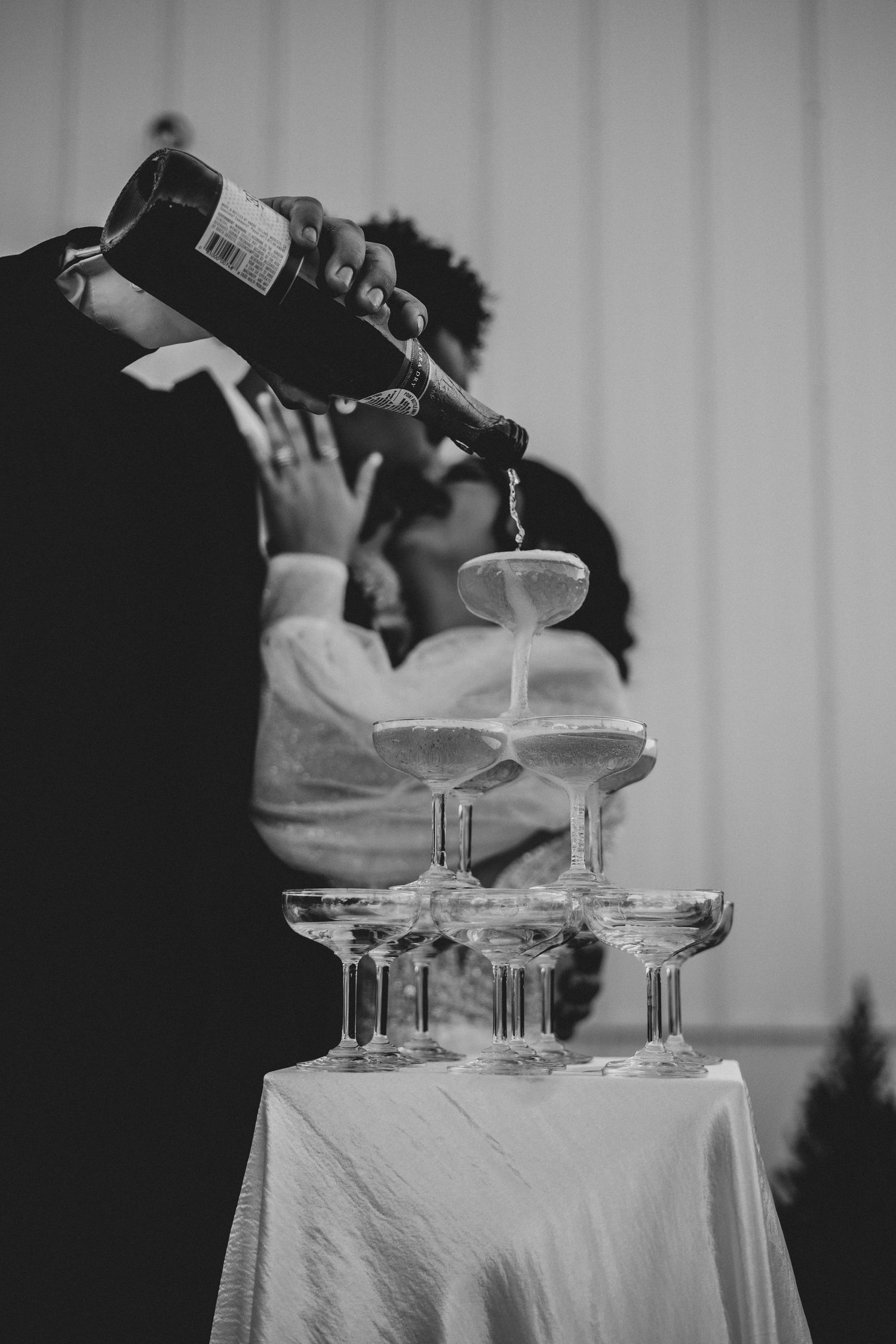 Black and white image of champagne being poured into tower of glasses.