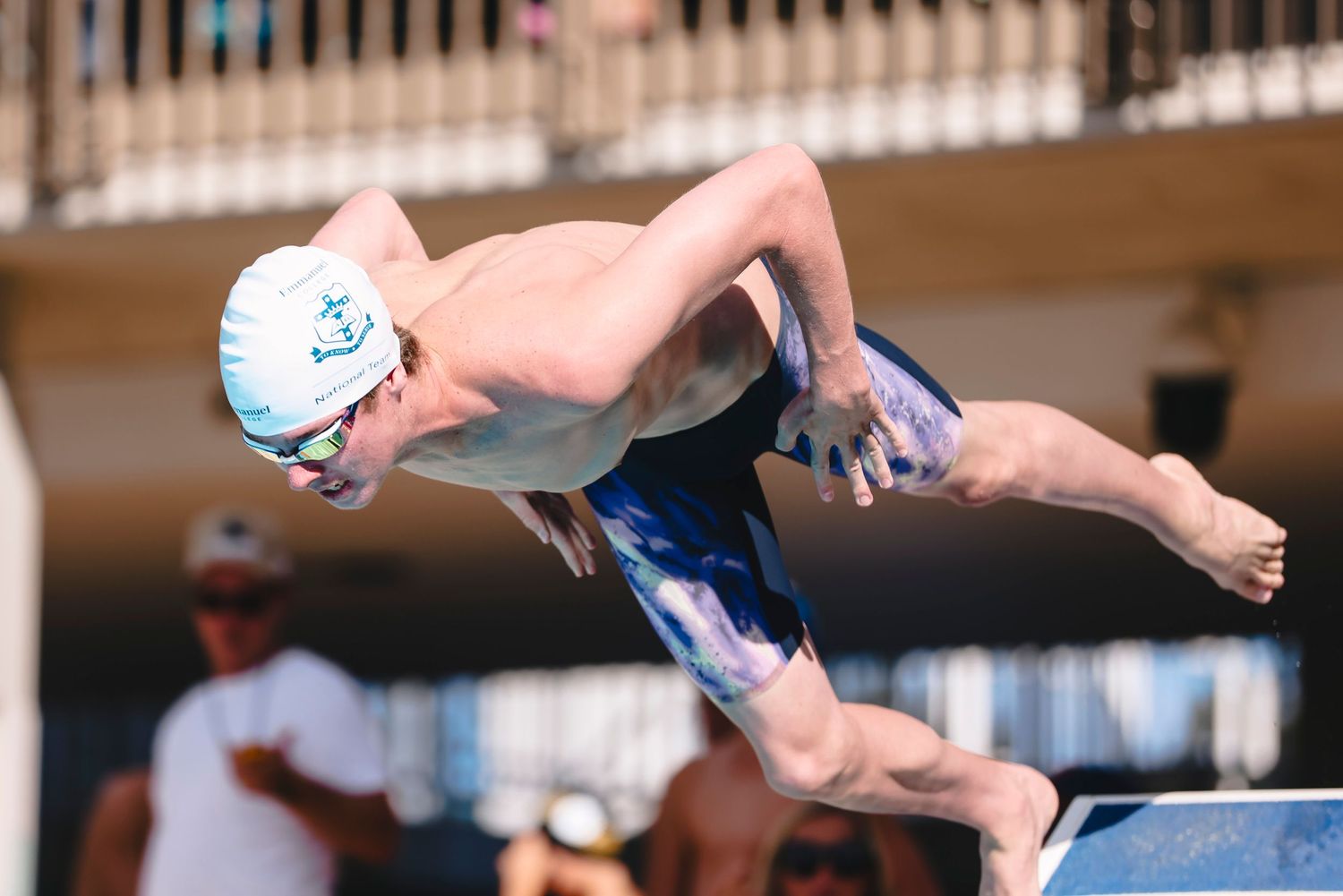 Competitive swimmer in blue swimwear executes a powerful dive into the pool during a race.