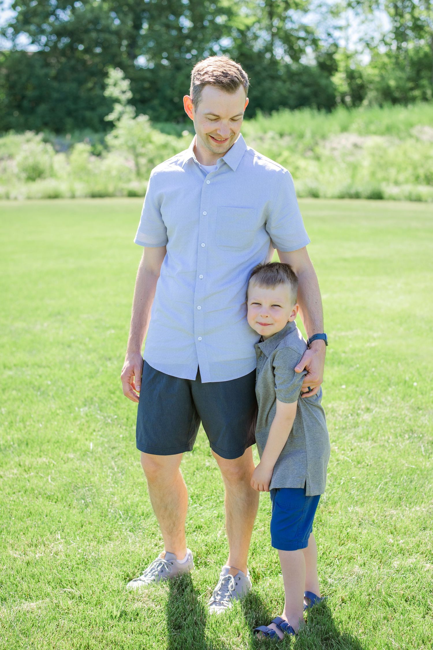 A father and son share a tender moment standing together in a sunny park.
