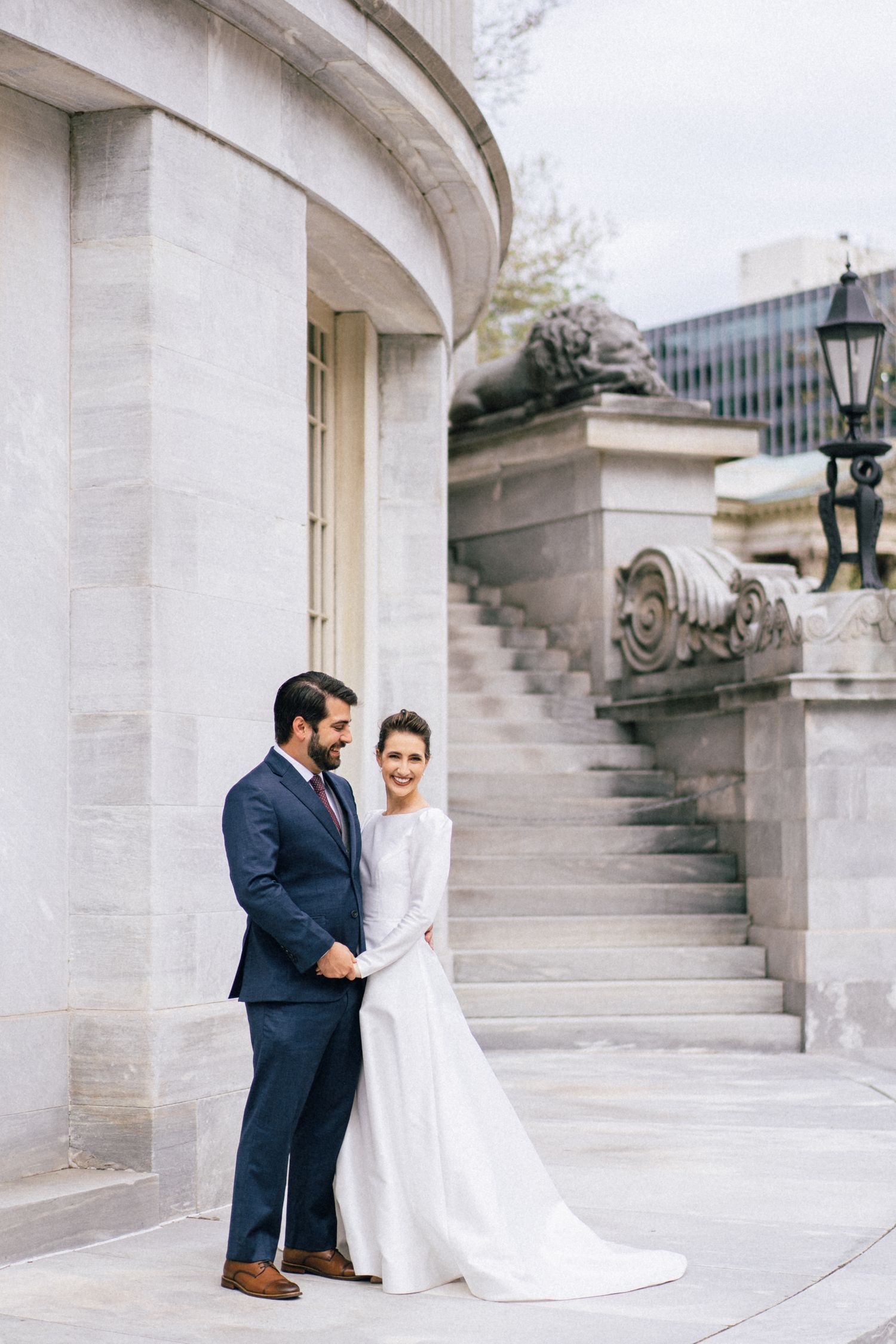Elegant couple in wedding attire standing together on classic stone architecture steps.