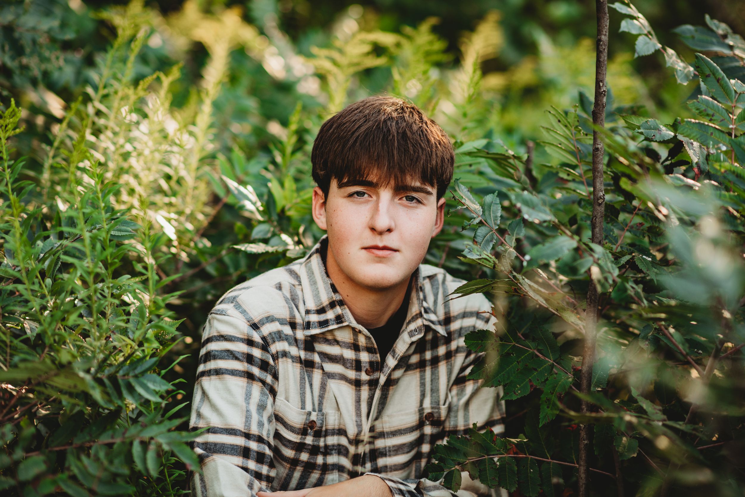 Portrait of someone in a plaid shirt surrounded by lush green foliage.