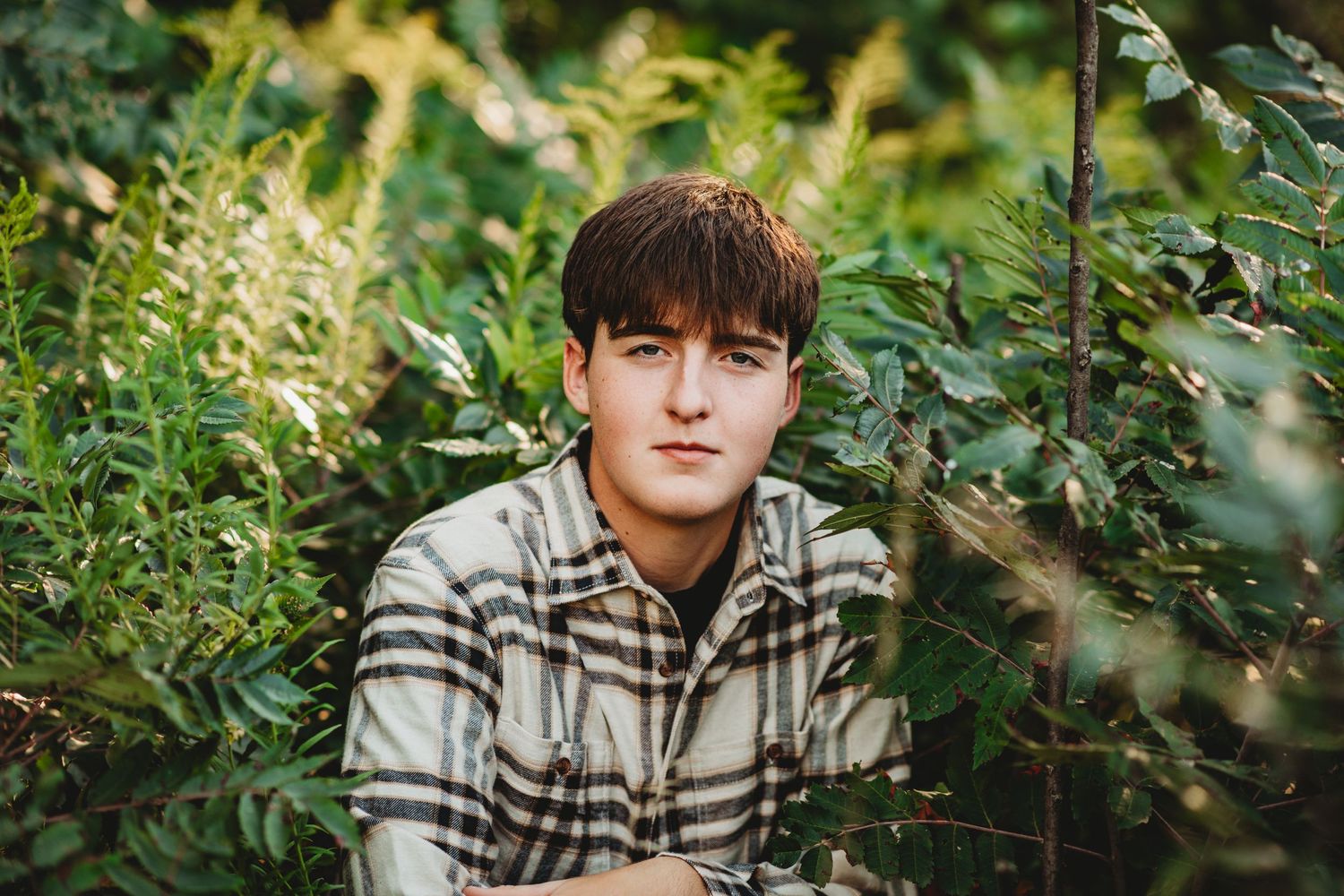Portrait of someone in a plaid shirt surrounded by lush green foliage.