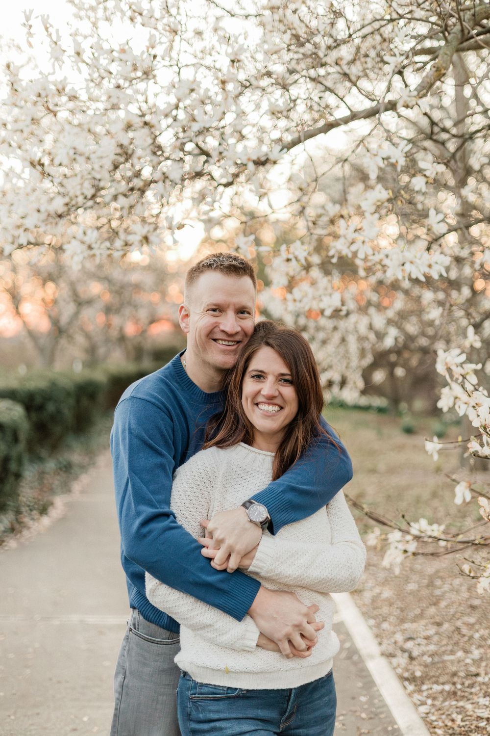 Engagement photos under blooming cherry blossom trees during golden hour.