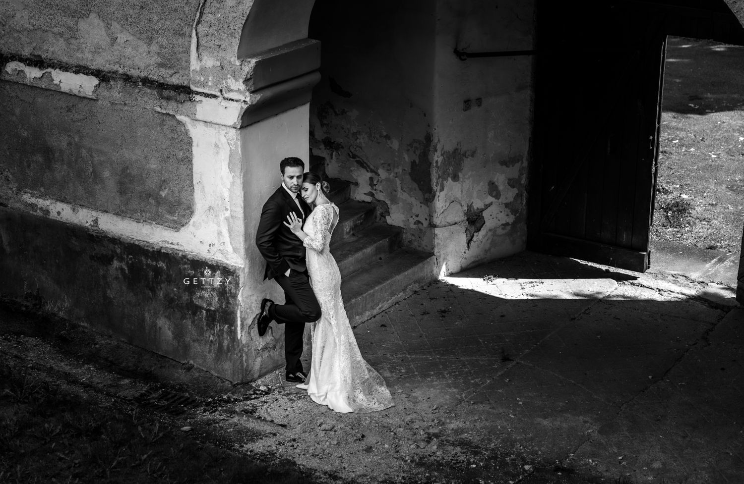 A romantic black and white wedding photo of a couple embracing in a stone archway.