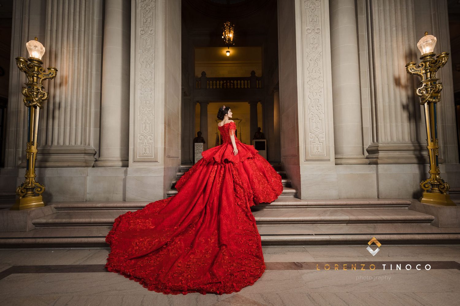 A dramatic red ballgown with a flowing train photographed on grand stone steps with vintage lighting.