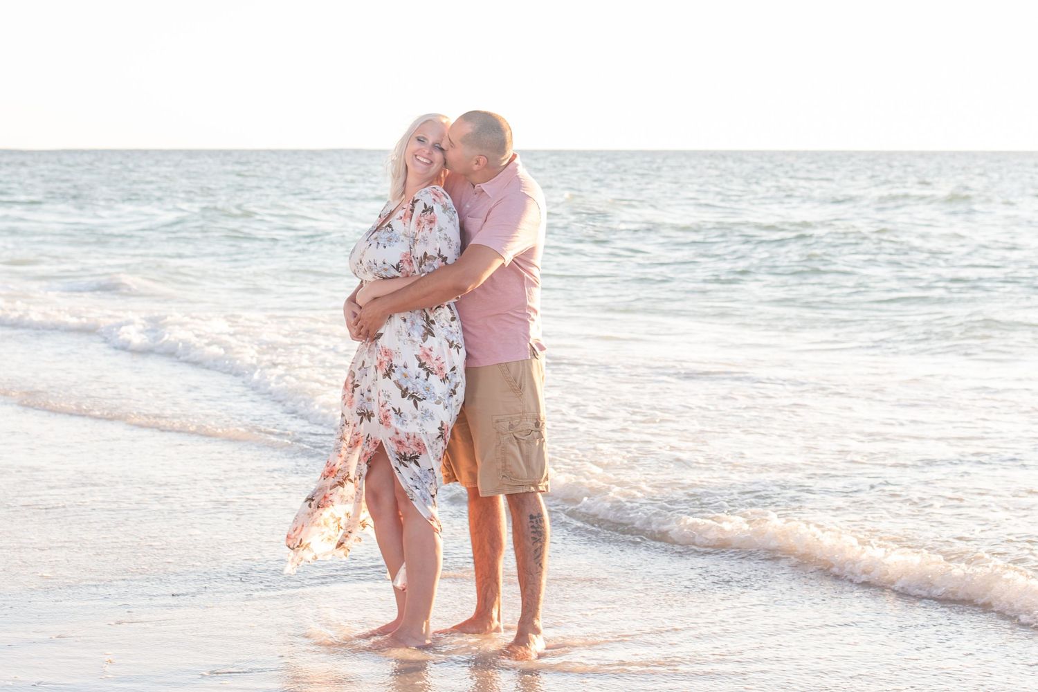Romantic beach photoshoot with couple standing in shallow ocean waves.