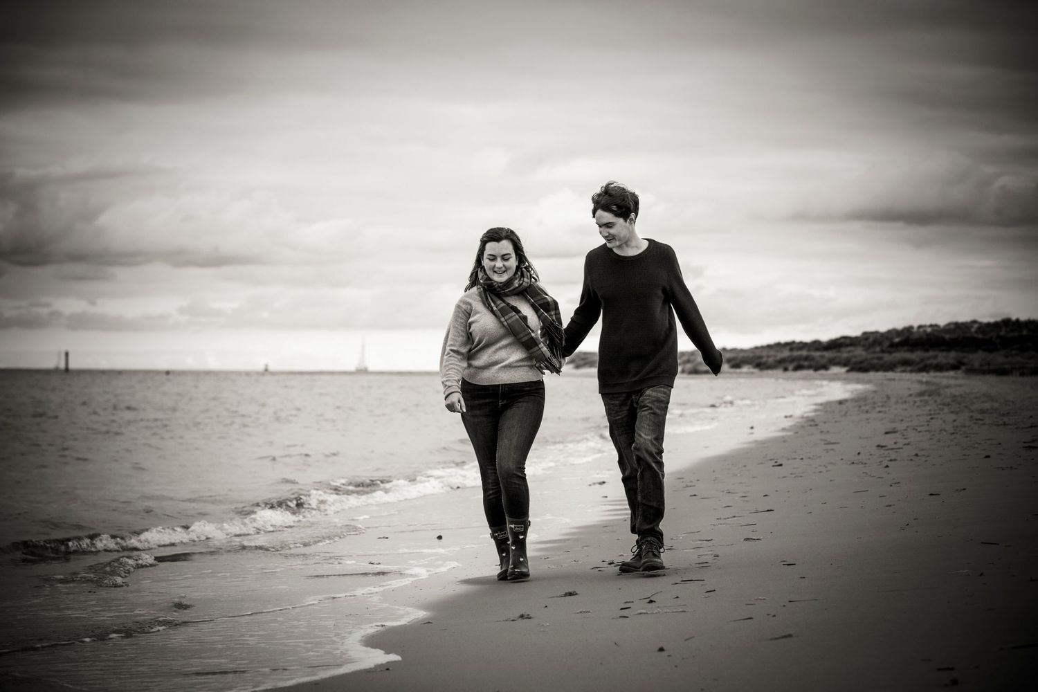 Couple walking hand in hand along a misty beach at sunset in black and white.