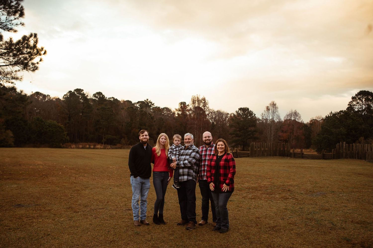 Family group poses together in open field at sunset.