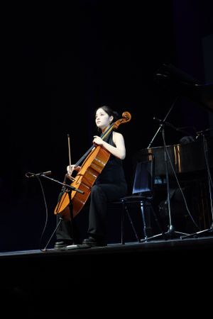 Professional cellist performing solo on stage in dramatic lighting.
