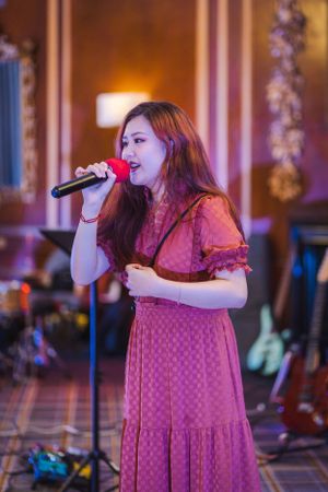Singer in a pink polka dot dress performs on stage with theatrical lighting in an elegant venue.