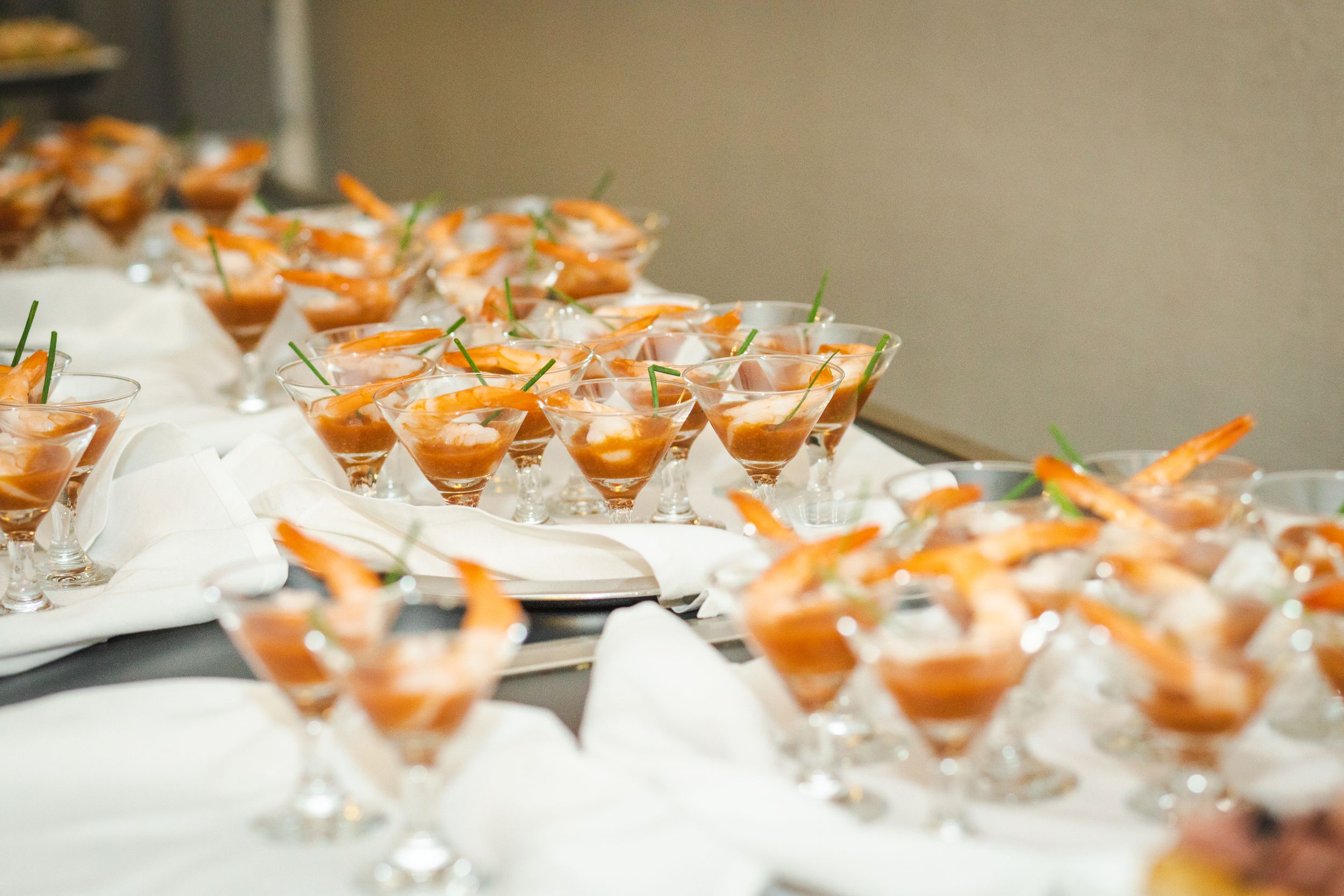 Martini glasses filled with shrimp cocktails arranged on a catering display table.