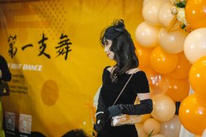 Person stands near decorative orange and white balloons with Chinese characters on yellow wall.