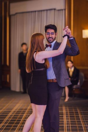 Dancing couple in formal attire performs in ballroom with patterned carpet.