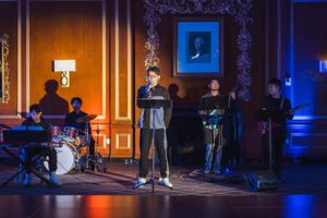 Dramatic stage lighting illuminates a performance space with silhouetted musicians in the background.