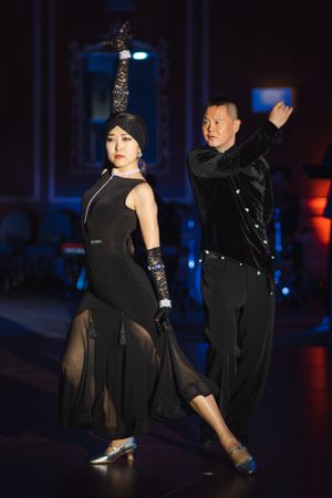 A couple performs a dramatic dance sequence in black attire under moody lighting.