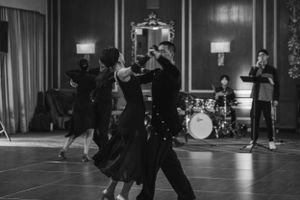 Dancers perform on a spacious hardwood floor with stage lighting and audience visible.