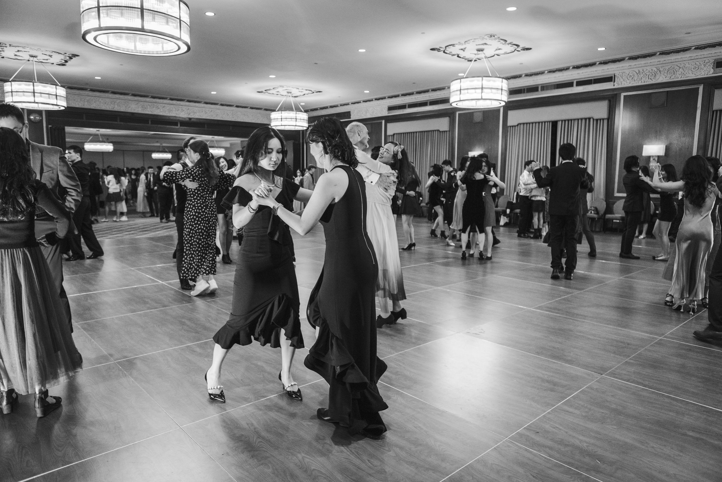 Wide angle view of an elegant ballroom with drum lighting and hardwood floors.