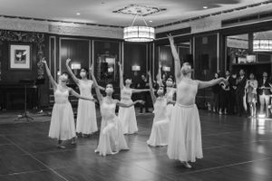 Dancers in formal attire perform synchronized movements in a spacious ballroom.