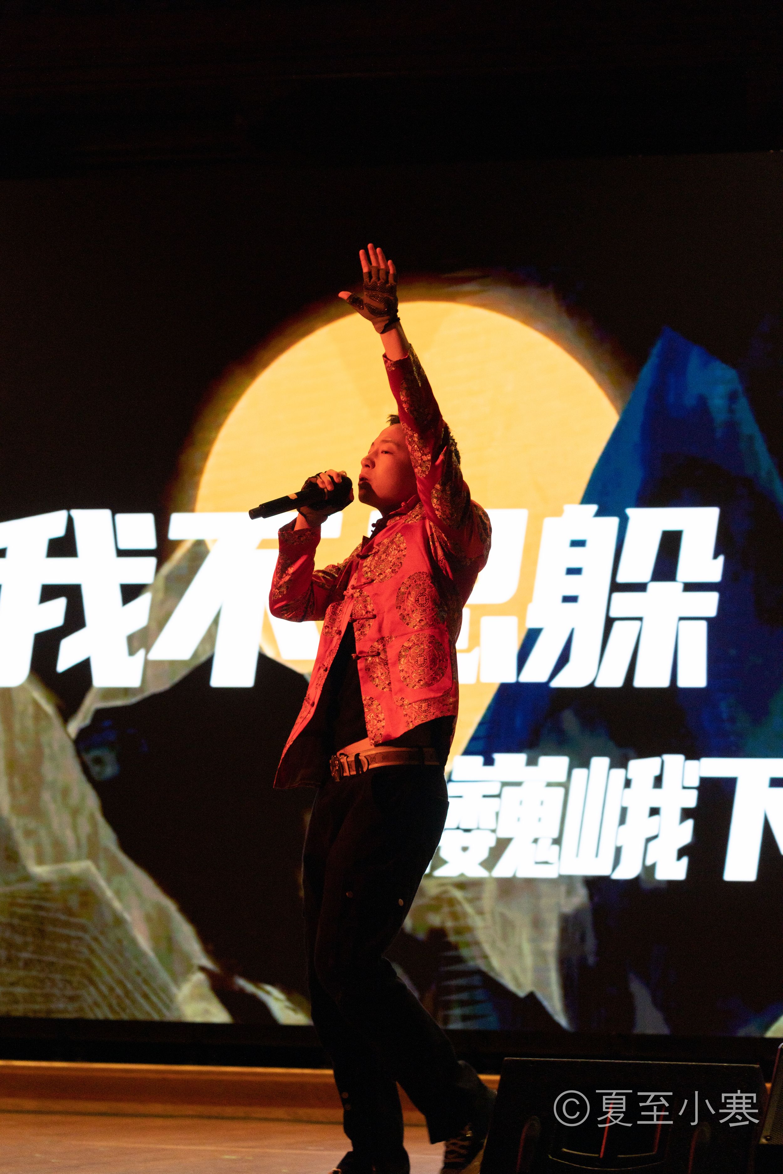 Performers silhouetted against large orange circle backdrop during stage production.