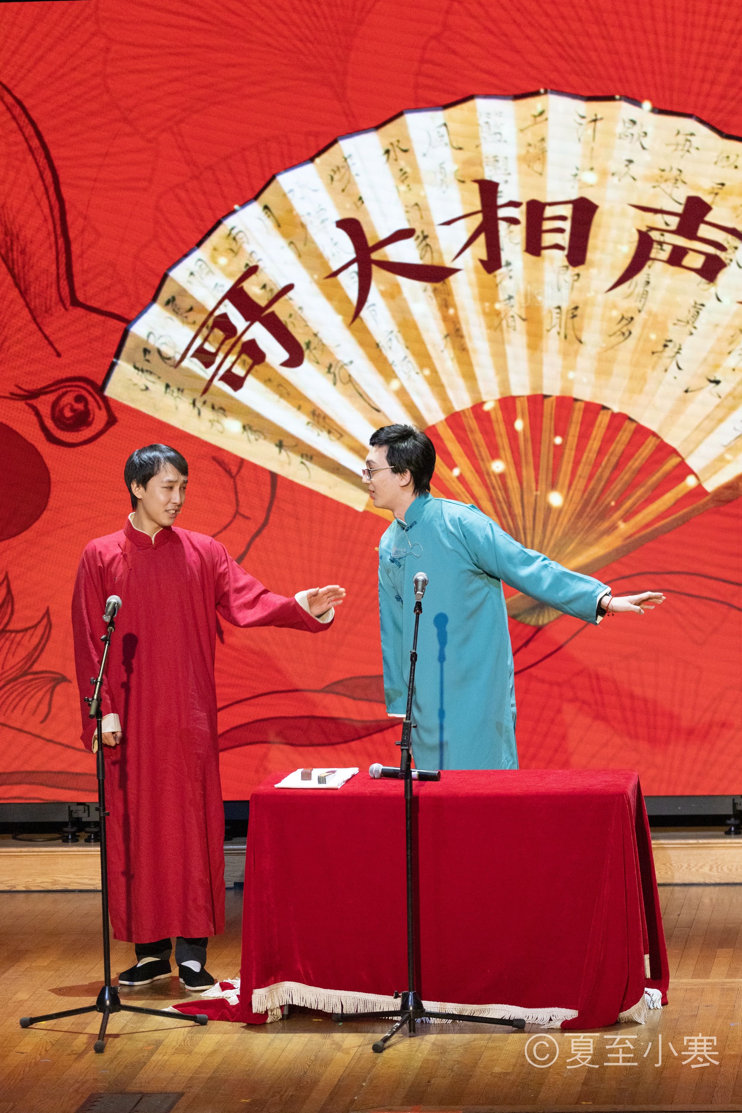 Traditional Chinese cross-talk comedy performance with performers in red and blue robes on stage.