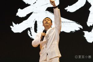 Performer in white outfit strikes dramatic pose against stark white background.
