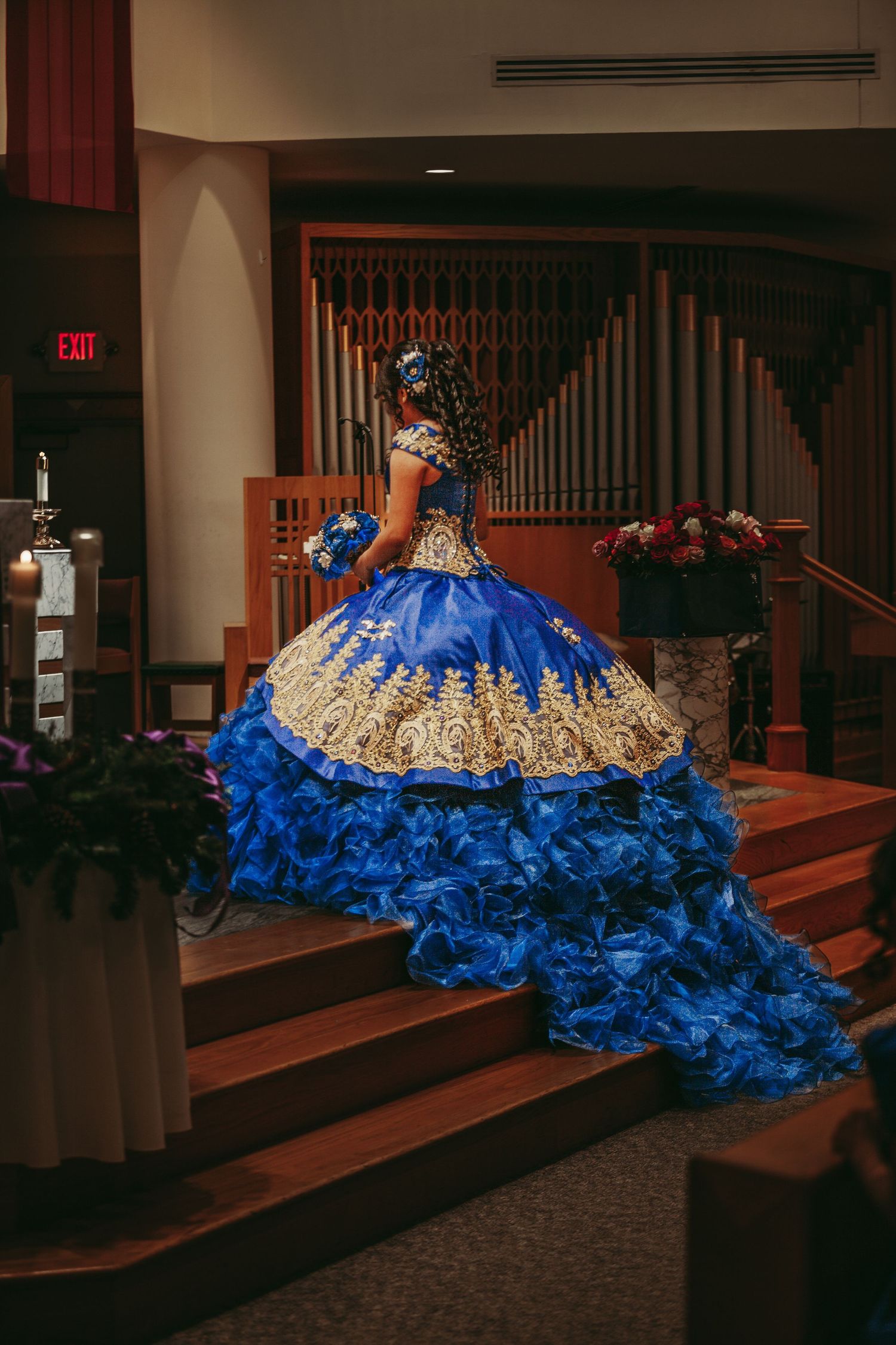 Dramatic royal blue and gold quinceañera dress displayed on church steps.
