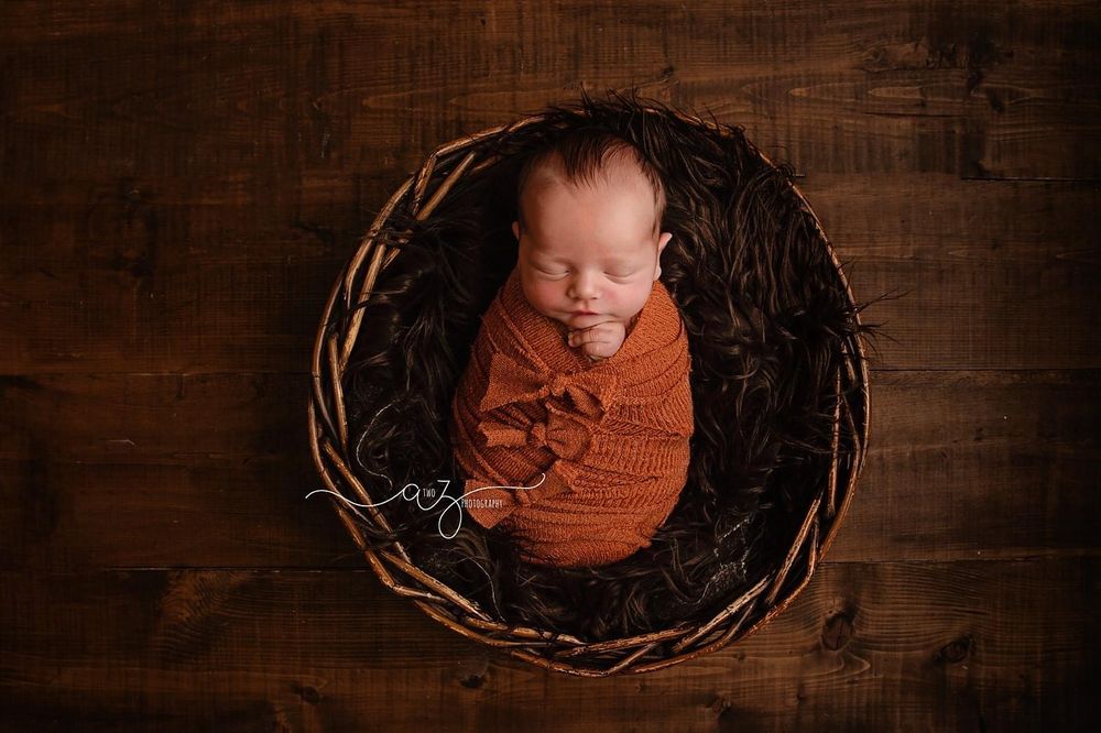 Overhead view of newborn wrapped in orange knit blanket in rustic woven basket.