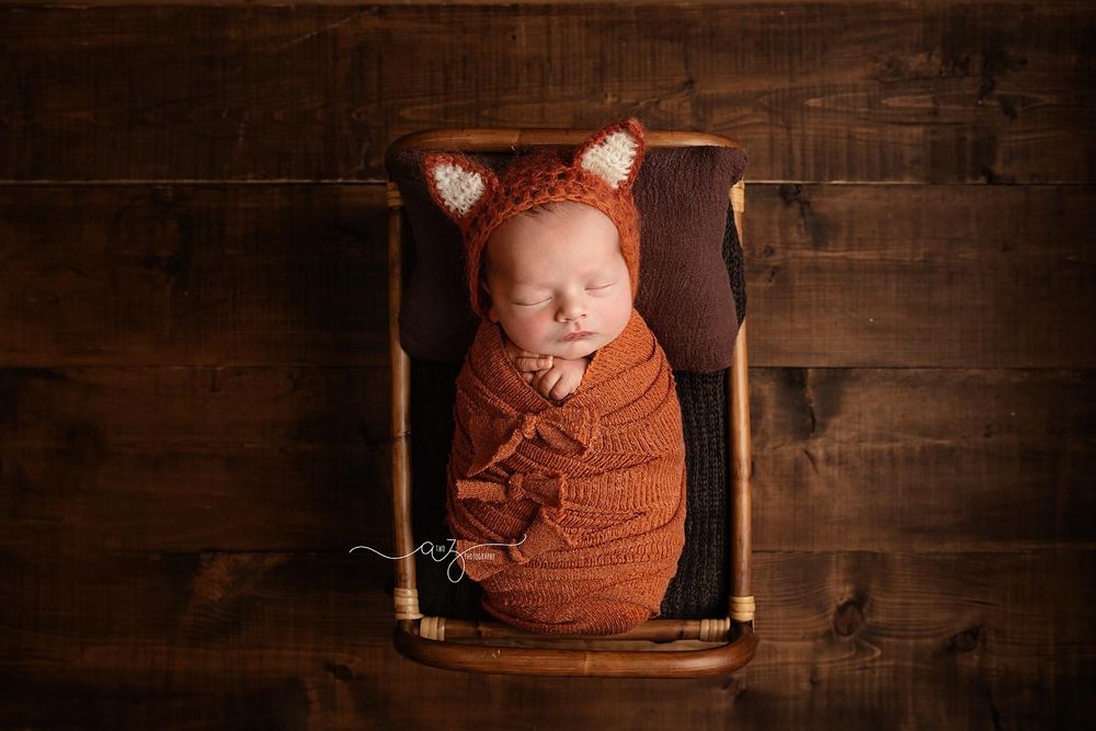 Sleeping newborn swaddled in rust-colored wrap lying in wooden box with rustic background.