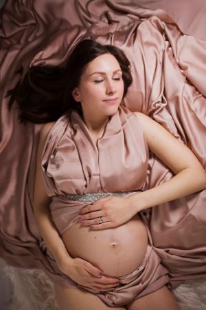 Glamorous maternity portrait aerial shot of mum to be on silky backdrop draped fabric