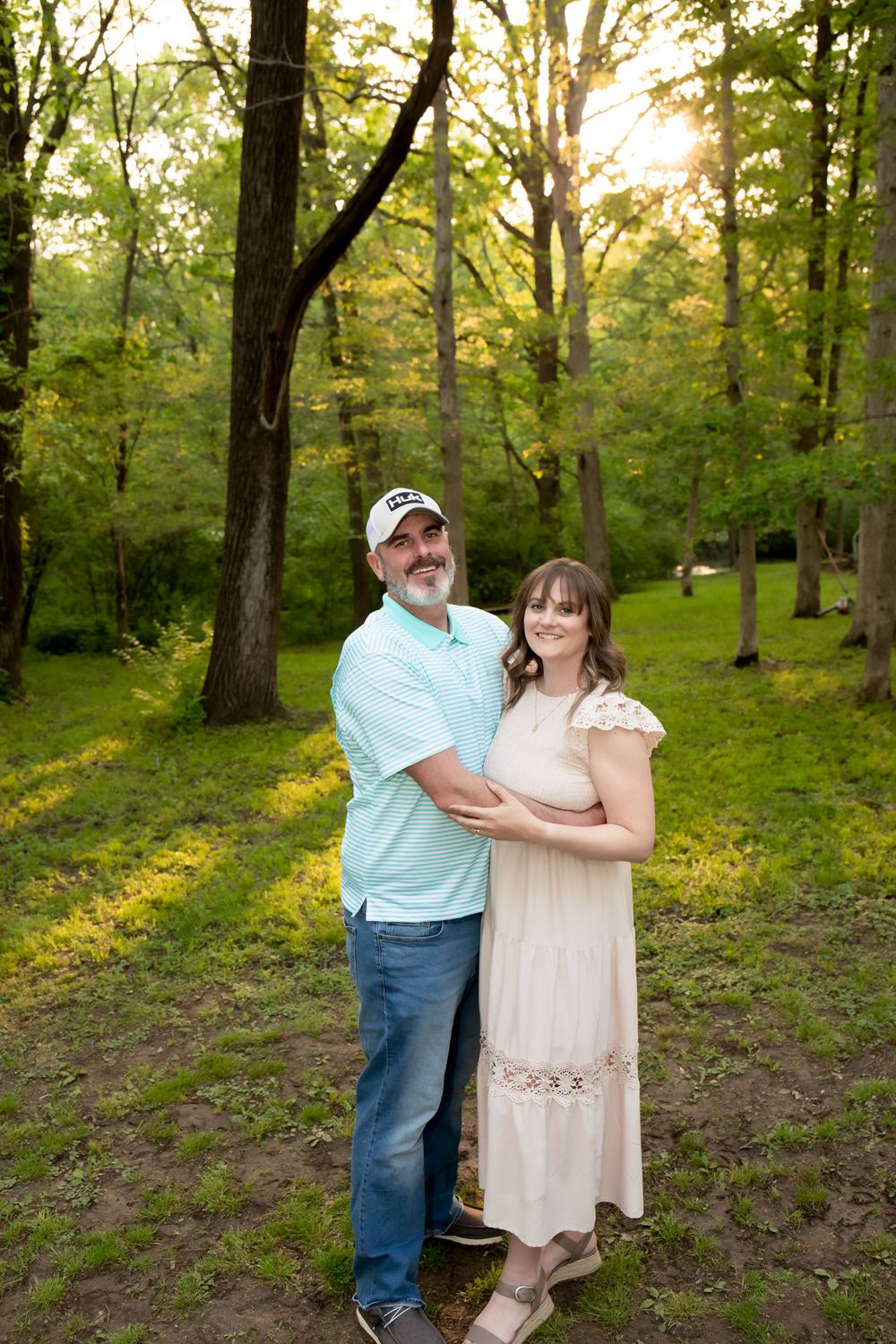 A couple poses together in a romantic forest setting at sunset.