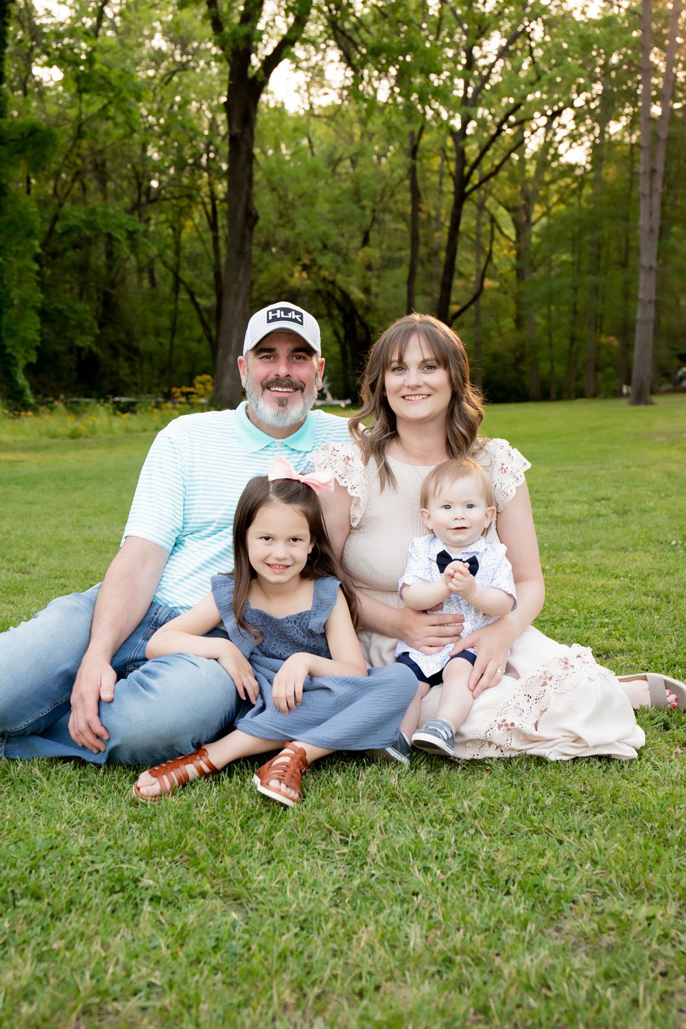 A family sits together for portraits in a wooded park setting at sunset.