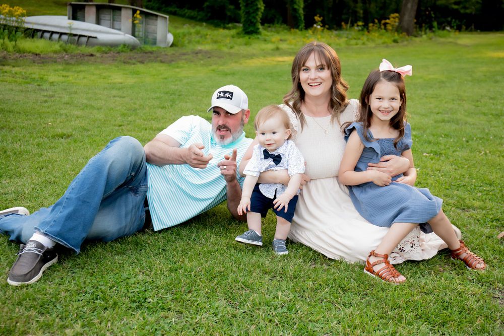 A family relaxes together on a grassy lawn during an outdoor portrait session.