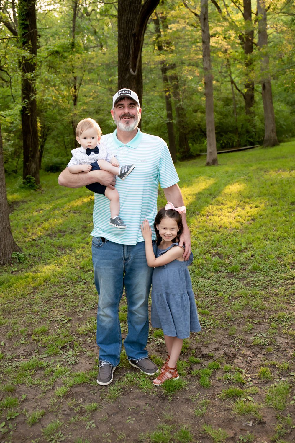 A family stands together in a lush green forest setting during a summer photo session.