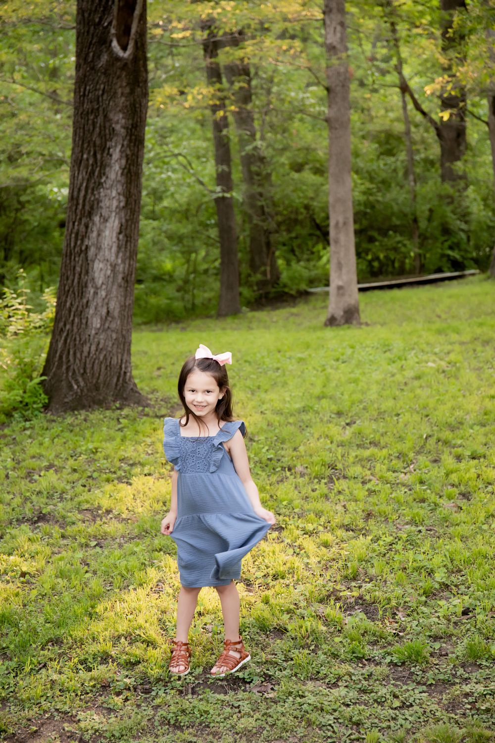 A child in a blue dress plays in a sunlit forest clearing.