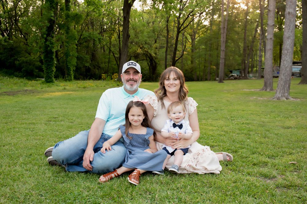 A young family poses together on green grass with trees in the background.
