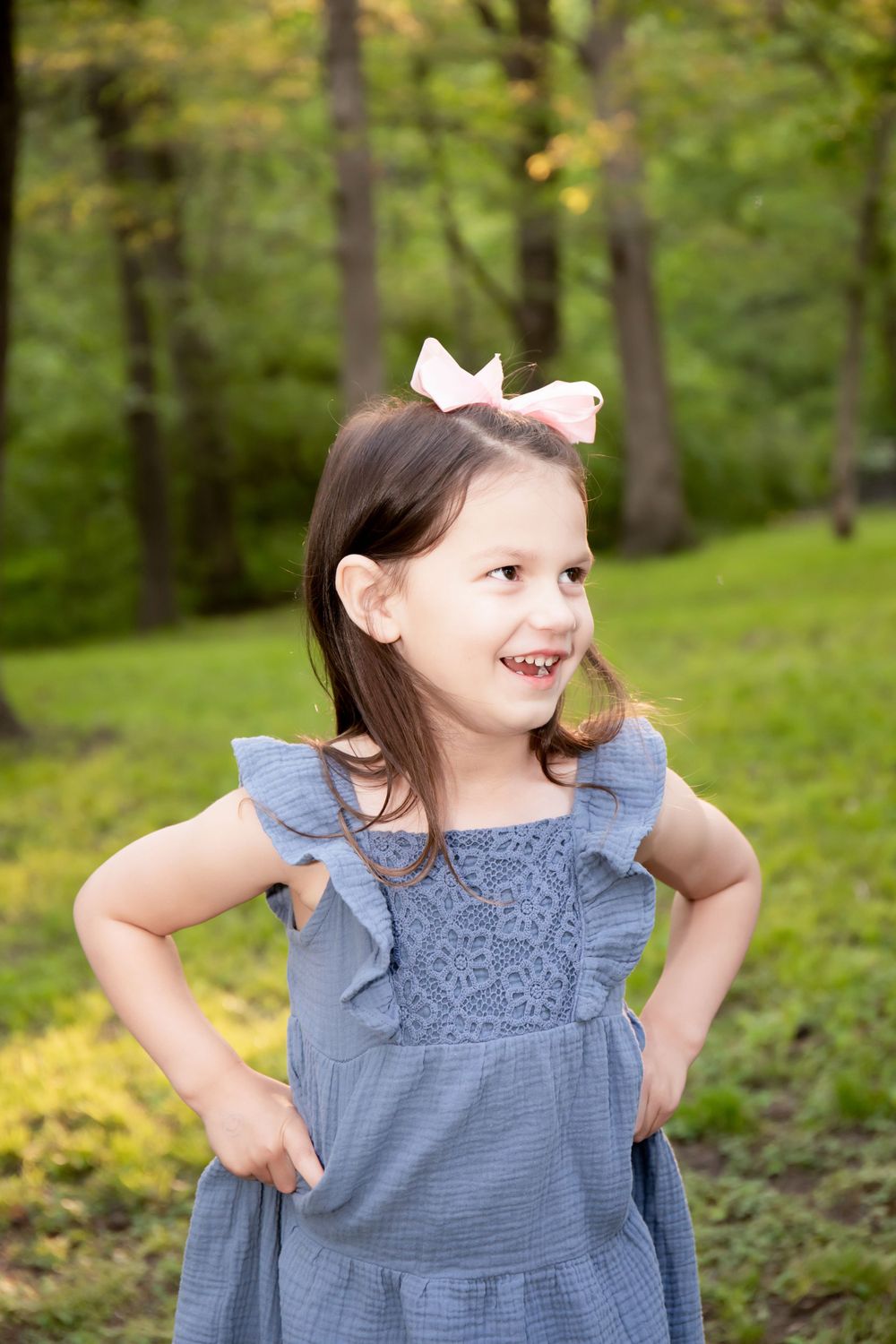 A joyful candid moment captured of someone in a blue dress with a white bow in the woods.