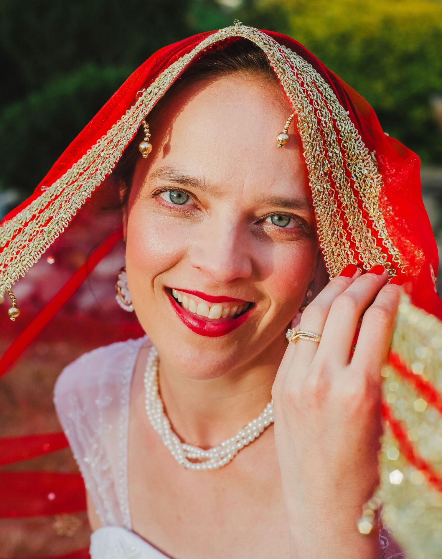 A bright red veil with gold embellishments frames elegant pearl jewelry.