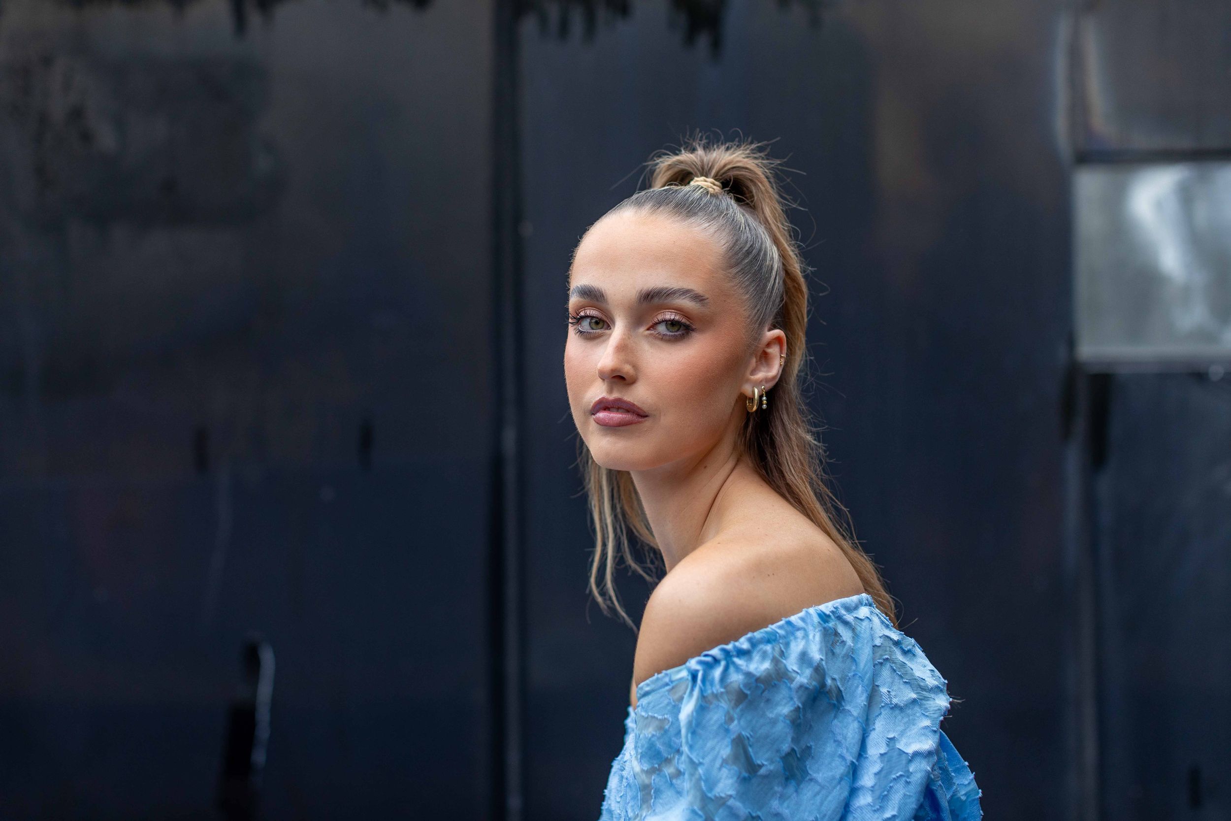 Fashion portrait against dark urban background in blue off-shoulder dress.