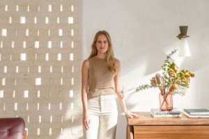 Bright modern interior with woman standing by window near decorative table with floral arrangement.