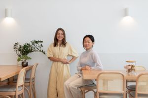 Two people posing in modern minimalist cafe with rattan chairs and white walls.