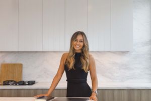 Modern white kitchen interior with woman smiling at counter.