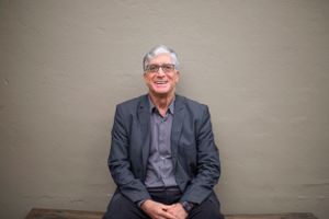 Professional sitting against grey wall wearing dark suit jacket.