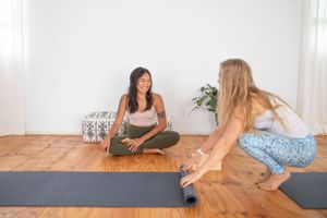 Two women sitting on yoga mats having conversation during wellness session.