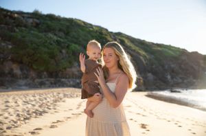 Mother and baby sharing a tender moment together on a sunny beach at sunset.