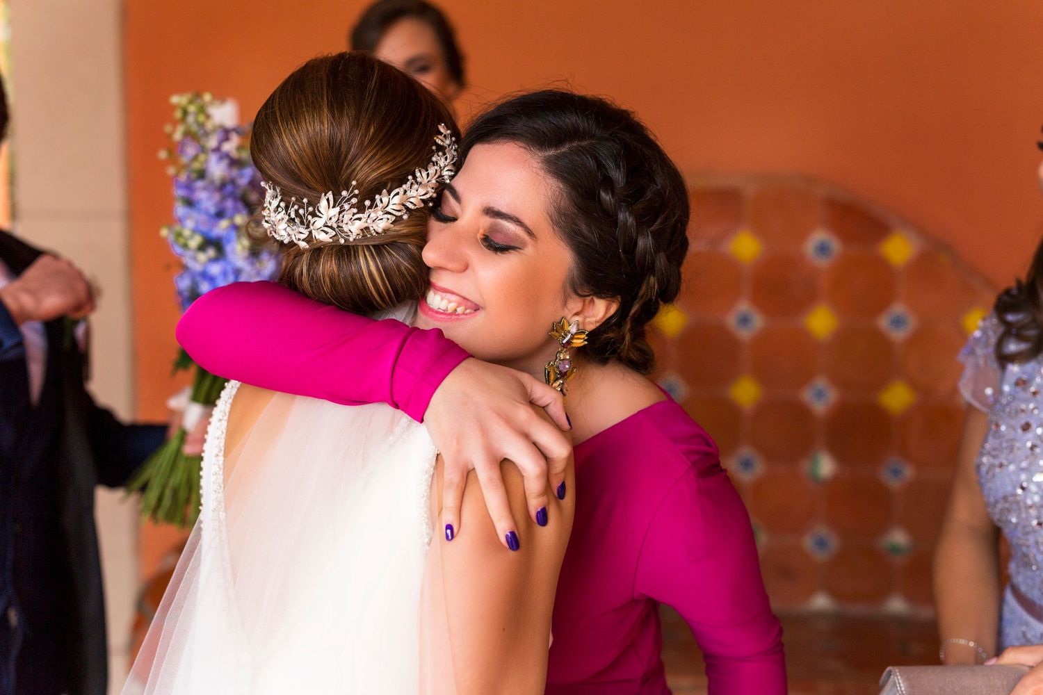 An emotional embrace shared during a wedding celebration against an orange wall.